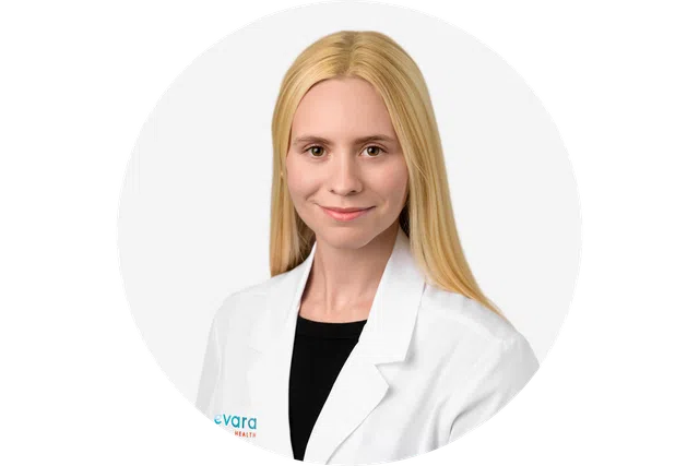 Smiling blonde female medical professional wearing white lab coat over black top on white background