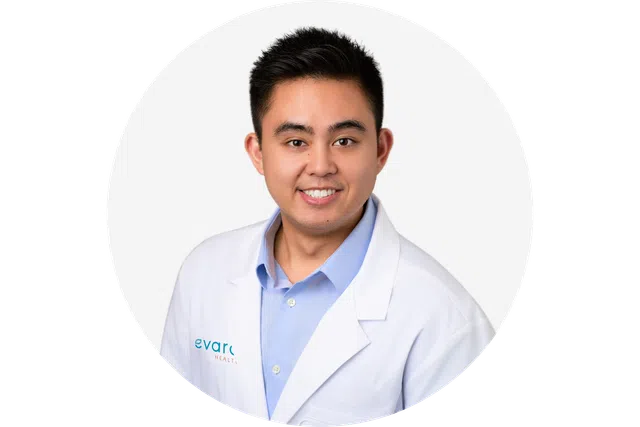 Smiling male doctor in light blue shirt and white lab coat with Evare Health logo on a white background.
