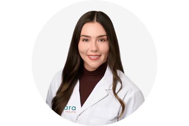 Young female healthcare professional with long brown hair wearing a white lab coat and maroon turtleneck smiling