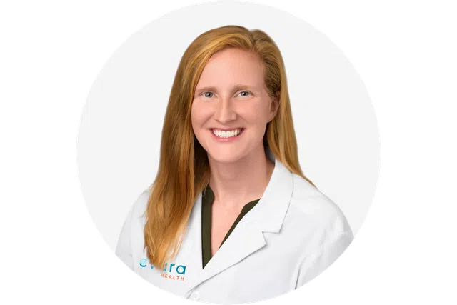 Smiling female medical professional with red hair wearing a white lab coat against a white background.