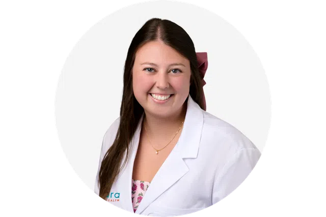 Smiling young woman wearing a white medical coat and floral blouse with long brown hair and necklace