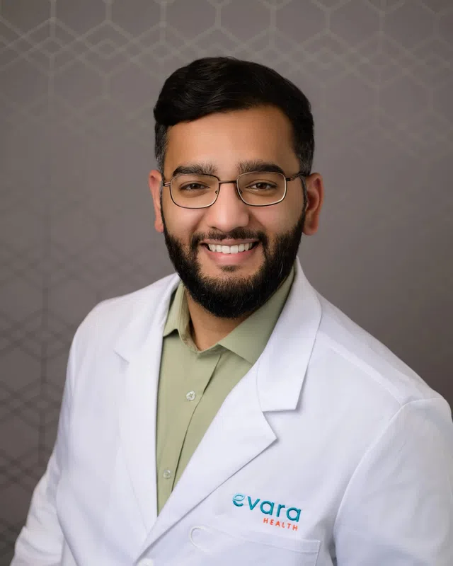 Smiling male healthcare professional wearing glasses and a white coat with Evara Health logo