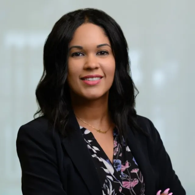Confident woman in a blazer with floral blouse, smiling with arms crossed in a professional setting.