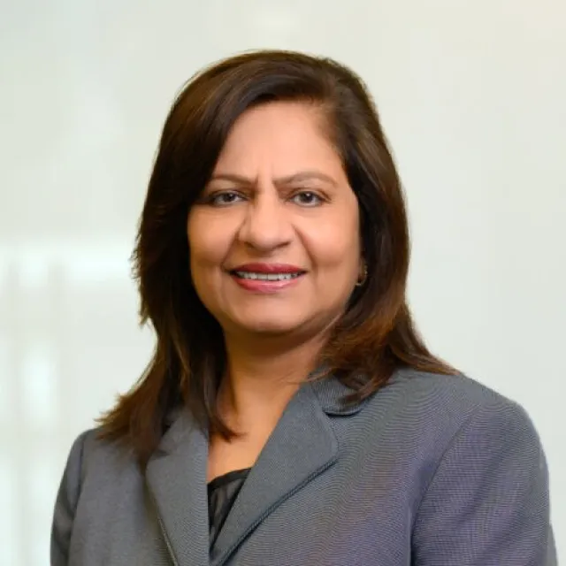 Professional woman in gray blazer smiling with shoulder-length brown hair and neutral background.