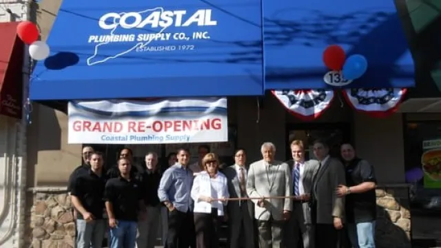 Coastal Plumbing Supply grand re-opening event with staff and guests at storefront under blue awning.