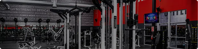 Modern gym interior with weightlifting equipment, machines, motivational wall text, and vibrant red accents.
