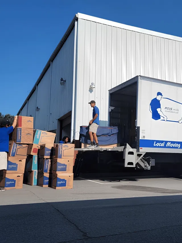 Moving truck being loaded with packed boxes by movers outside a warehouse on a clear sunny day