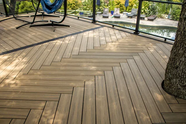 Outdoor Composite deck with herringbone pattern, hammock chair, and pool view surrounded by greenery and lounge chairs Marietta, GA.