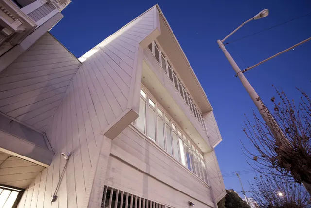 Modern white building with large windows and angled roof against a clear evening sky with streetlight.