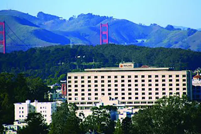Golden Gate Bridge visible behind a large hospital building amidst green hills and trees in San Francisco