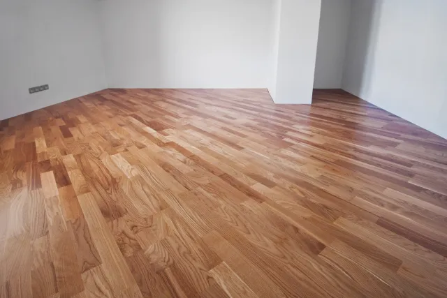 Empty room with polished natural wood flooring and white walls in bright natural light.