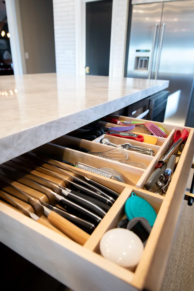 Open kitchen drawer neatly organized with knives, utensils, and cooking tools in wooden compartments.