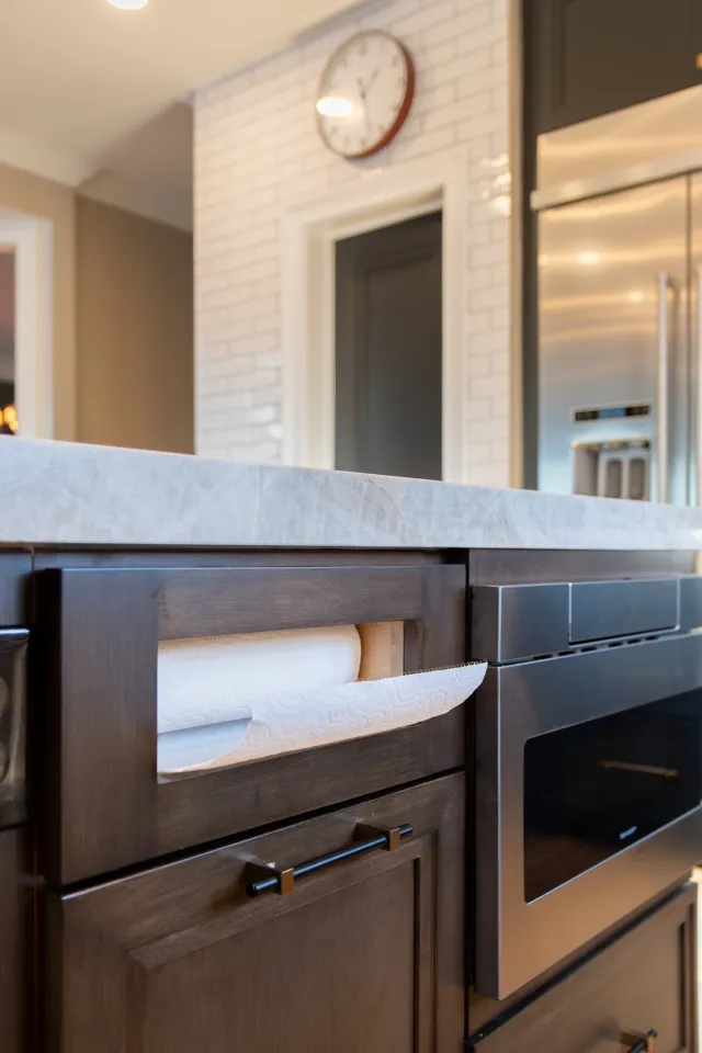 Modern kitchen with built-in paper towel holder, dark wood cabinets, marble countertop, and stainless steel oven.
