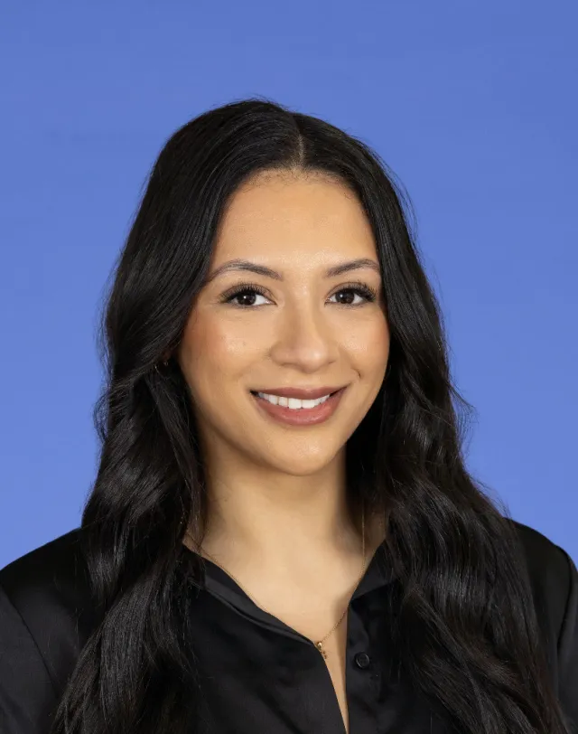 Smiling woman with long dark hair wearing a black blouse against a blue background.
