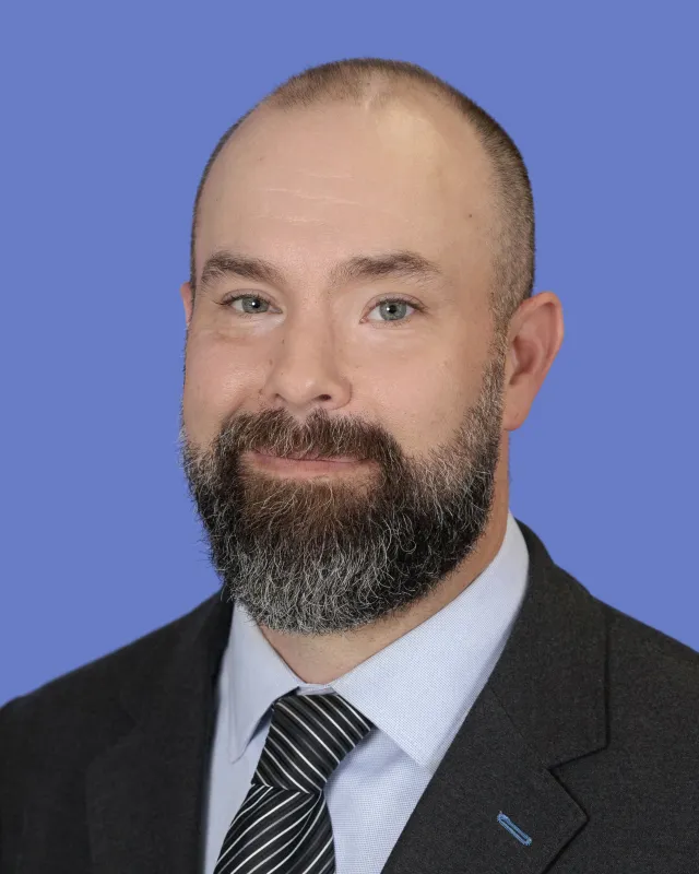 Smiling bald man with gray beard in business suit and striped tie on blue background