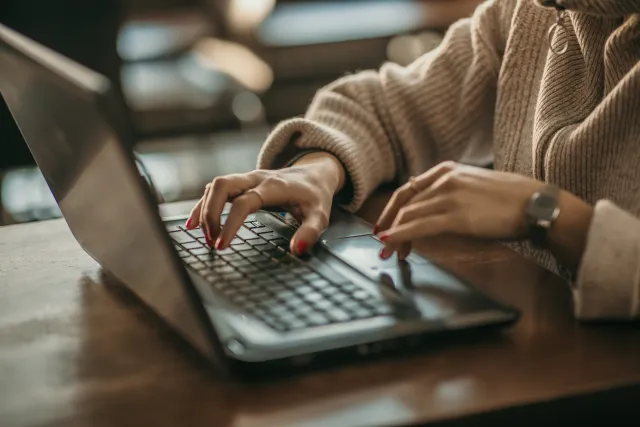 Close-up of a person typing on a laptop in a cozy coffee shop setting with soft lighting.