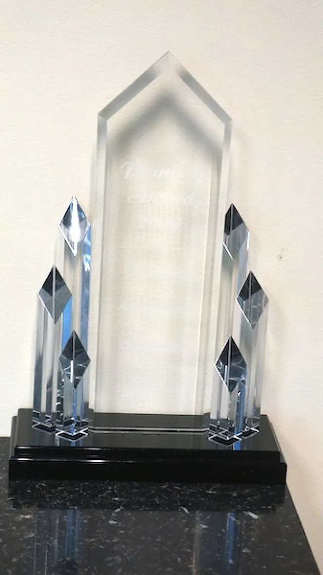Clear glass award trophy with multiple crystal pillars on a black base against a white wall.