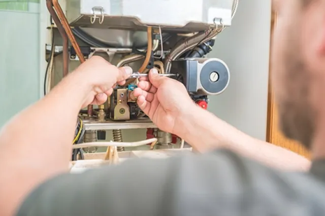 Technician repairing a boiler system using a wrench on copper pipes inside a utility room.