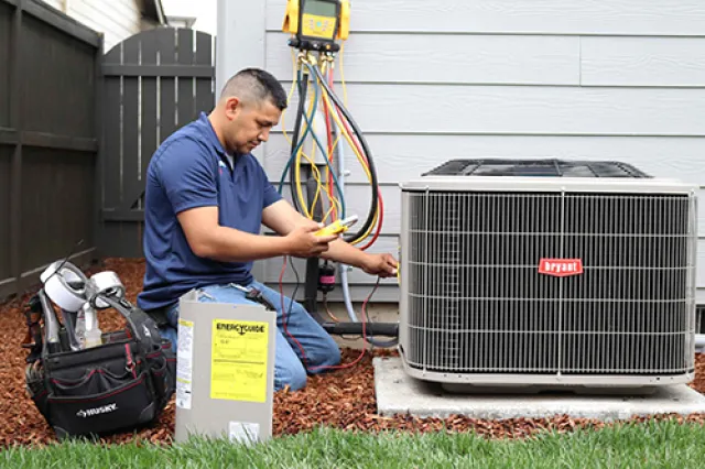 Technician repairs and tests a Bryant air conditioning unit outside a house with HVAC tools and gauges