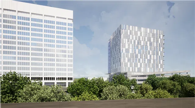 Modern office buildings with reflective glass facades behind green trees under a partly cloudy sky.