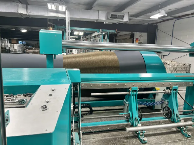 Industrial textile machine winding brown yarn onto a large spool in a factory setting