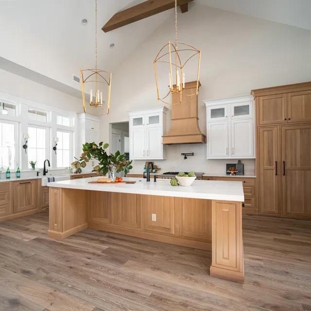 Bright modern kitchen with wood cabinetry, large island, white countertops, pendant lights, and vaulted ceiling beams.