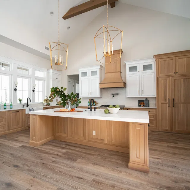 Modern kitchen with vaulted ceiling, wooden cabinets, white island countertop, and gold pendant lights