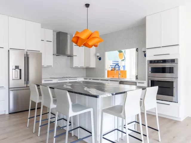 Modern white kitchen with black marble island, stainless steel appliances, and distinctive orange pendant light.