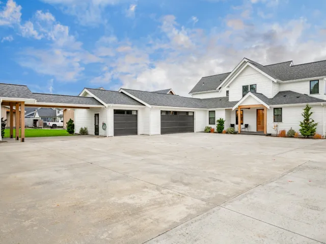 Modern white two-story house with multiple gray garage doors and large concrete driveway under a blue sky.