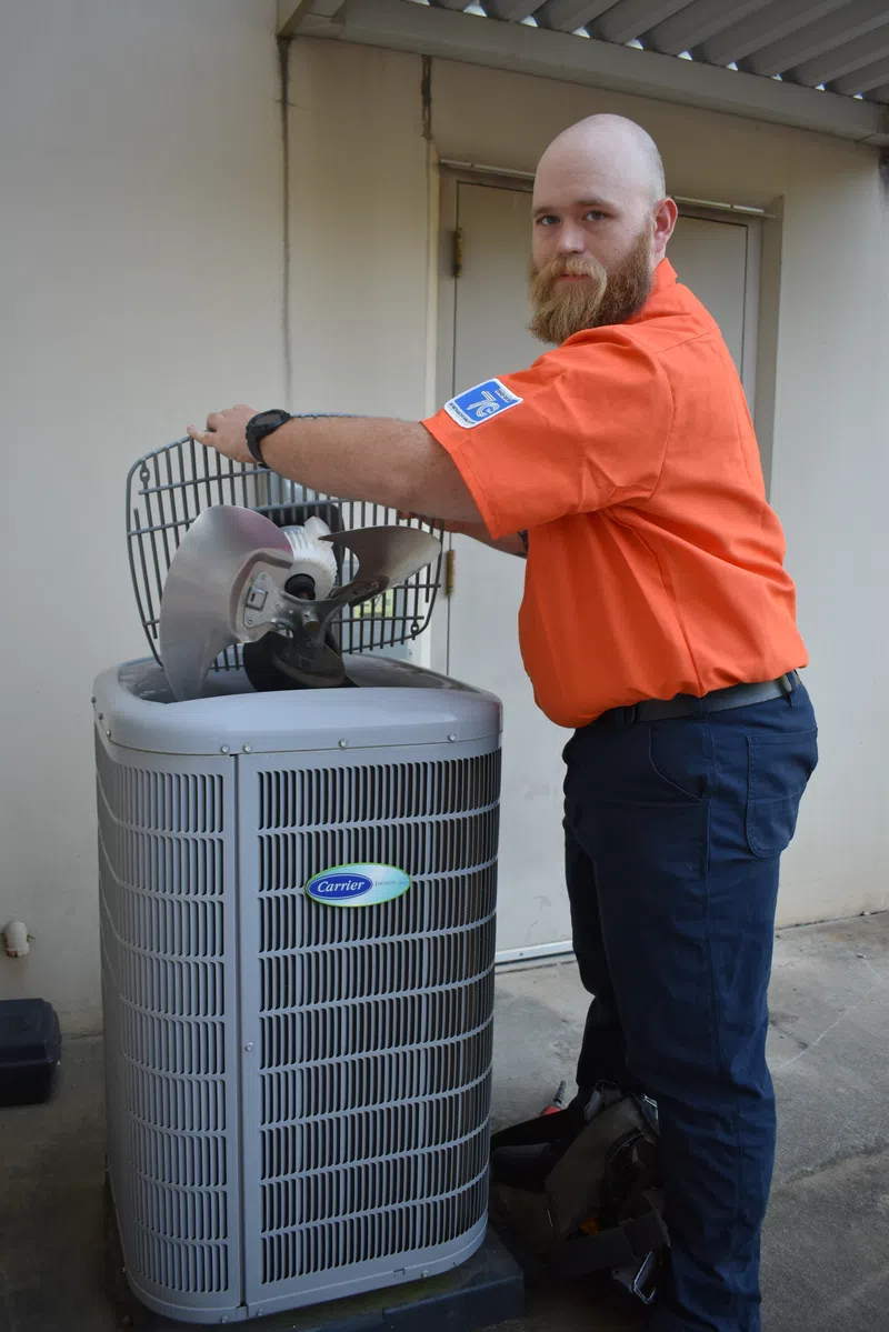 Estes Services Technician in orange shirt fixing Carrier air conditioning unit with open top exposing the fan blades outdoors.