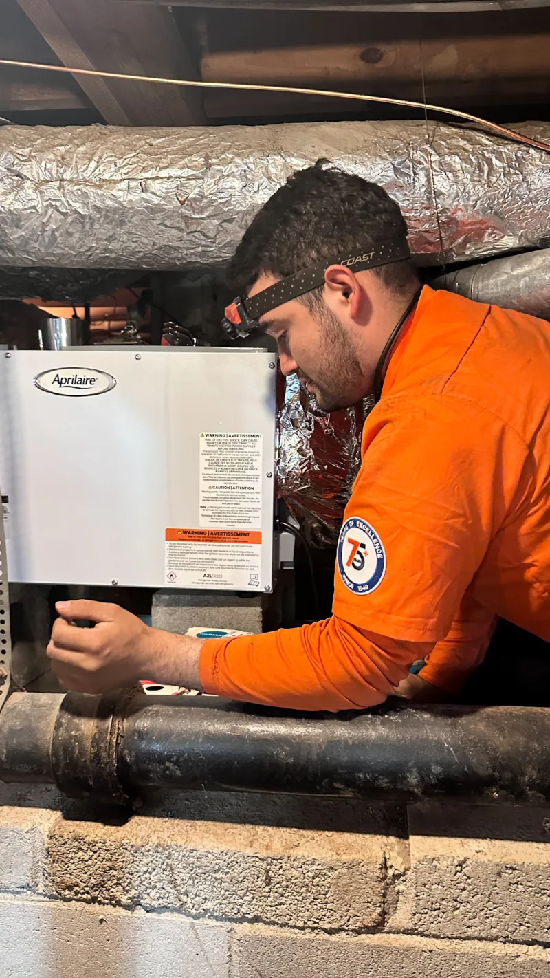 Estes Services Technician in orange shirt uniform installing a Dehumidifier April Air in a basement