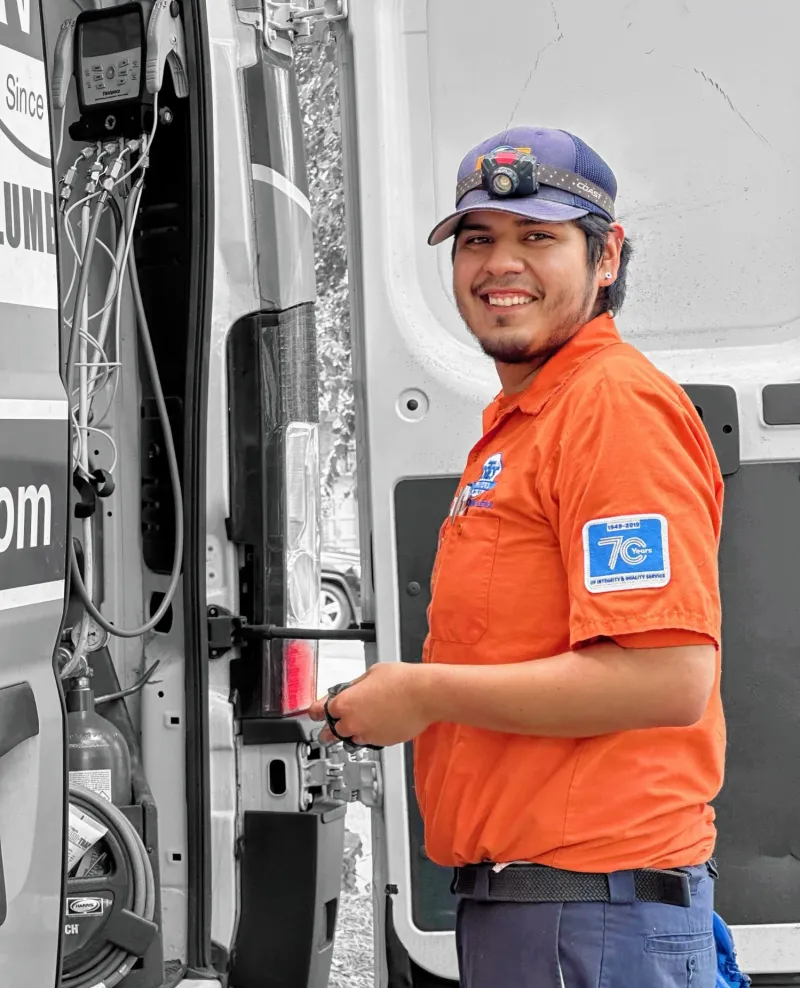 Smiling plumber in orange shirt and headlamp working near open service van door