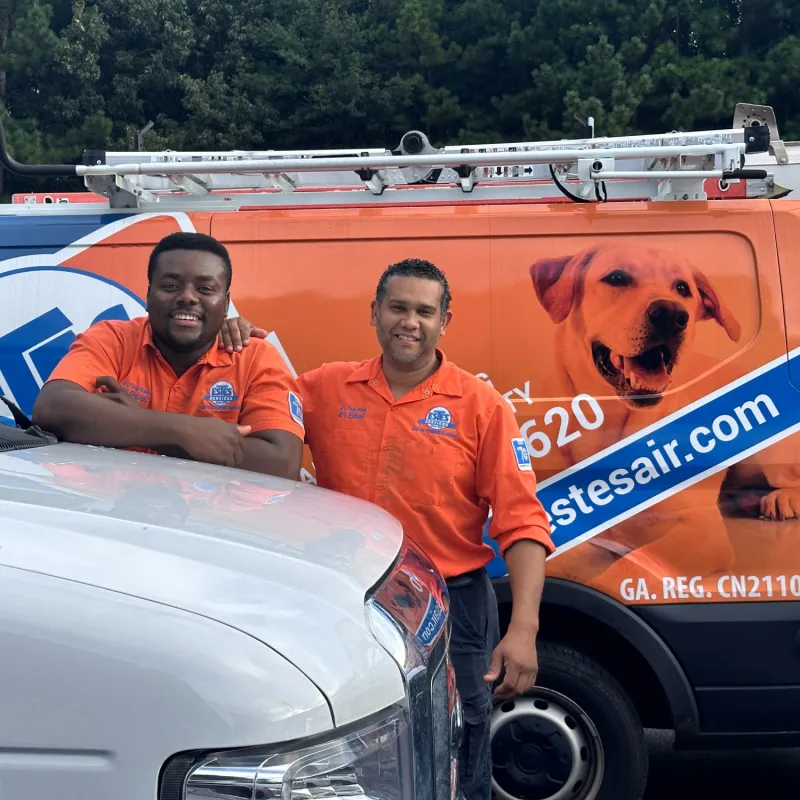 Two Estes  technicians in orange uniforms smiling in front of a Estes Services van with a dog image and company website.