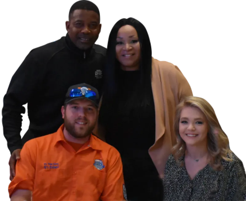Group portrait of four smiling adults, two standing and two sitting, dressed in casual and work attire indoors.