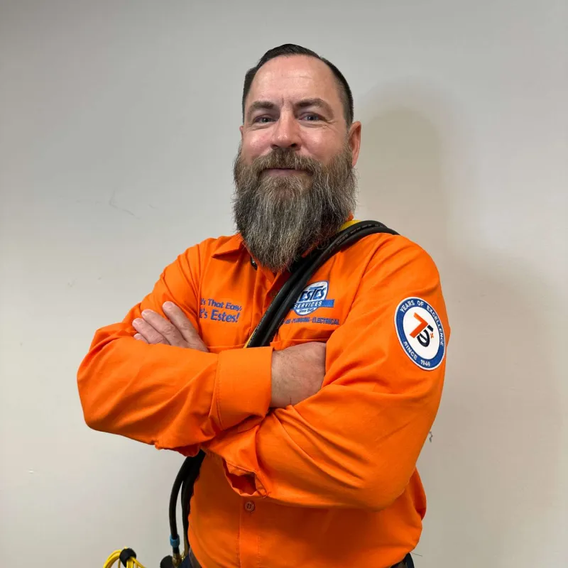 Estes Services Tech man with crossed arms wearing an orange work shirt with company logos and holding black cables.