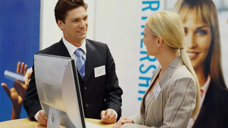 Booth staffer talking with a visitor at a trade show exhibit reception counter