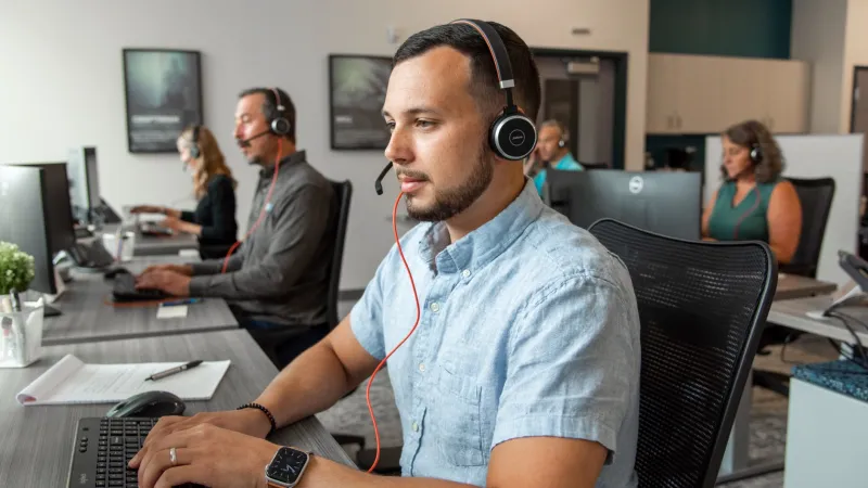 a man wearing headphones and sitting at a desk with other people