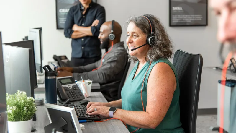 a woman wearing headphones and sitting at a desk with a laptop