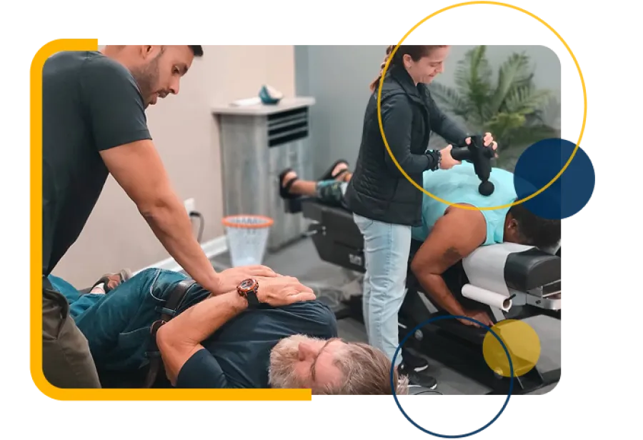 Chiropractor adjusting patient on table while another patient receives massage therapy with percussion device.