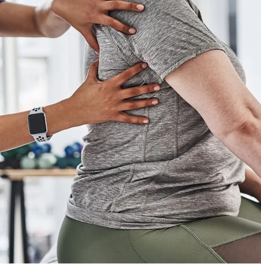 Physical therapist assists patient with back alignment during rehabilitation session indoors.