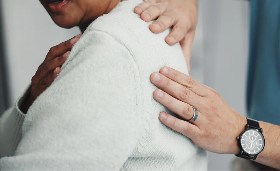 Therapist providing shoulder support and comfort to patient wearing white sweater in a counseling session.