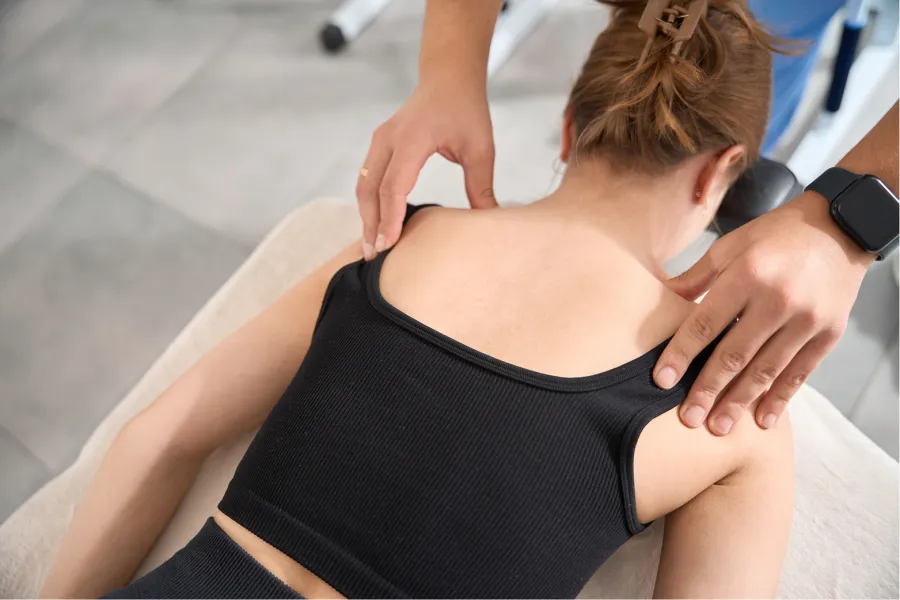 Woman receiving shoulder massage therapy on a treatment table wearing a black tank top in a clinic.