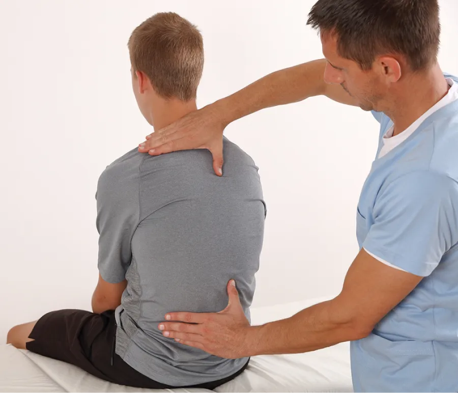 Chiropractor adjusting a boy's back during a treatment session in a clinic setting.
