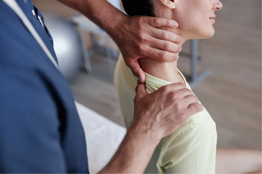 Chiropractor adjusting a woman's neck and shoulder during a physical therapy session indoors.