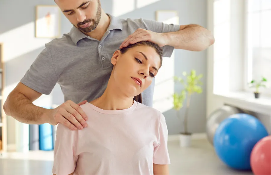 Physical therapist helping woman stretch and relieve neck pain in a bright therapy room with exercise balls.