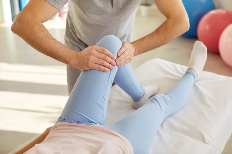 Physical therapist performing knee manipulation therapy on patient wearing blue leggings on treatment table.