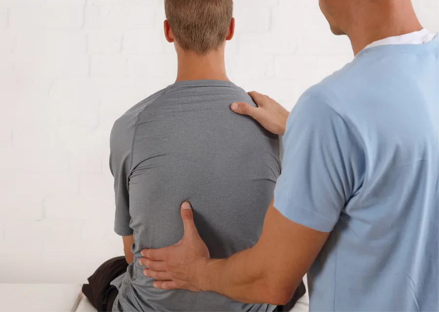 Physical therapist examining patient's back with hands for posture or pain assessment.