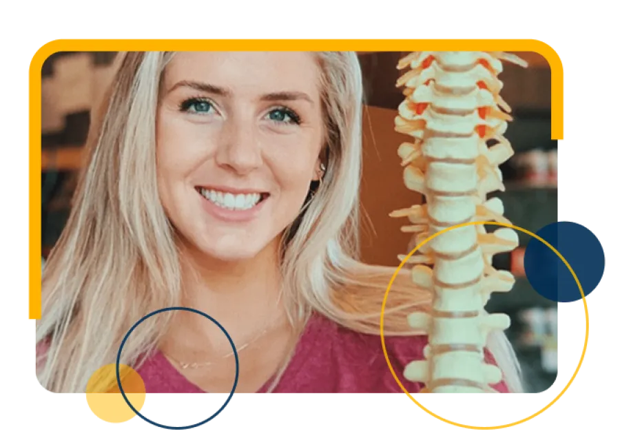 Smiling woman with blonde hair holding a model of a human spine in a medical or wellness setting