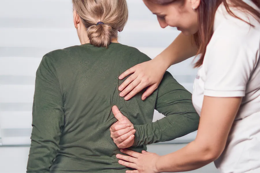 Physiotherapist assisting woman with back pain during a therapy session in a clinical setting