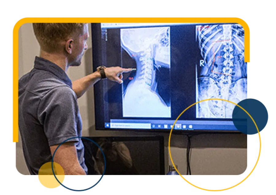 Doctor reviewing and pointing at spinal X-ray images on a large screen in a medical office setting
